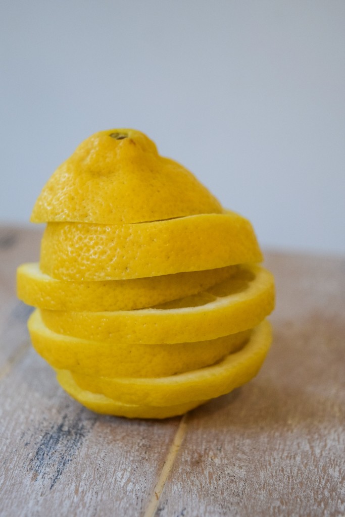 a lemon cut into 7 slices stacke ontop of each other to make a complete lemon sitting on a light tan washed wooden plank