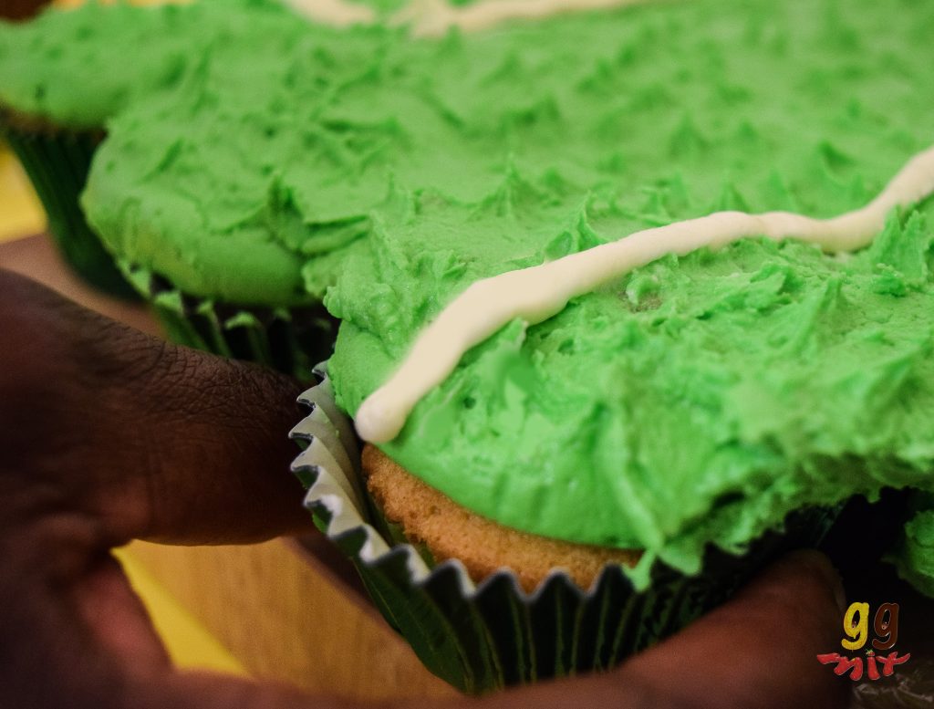 a hand pulling a cupcake out from a pullapart cke with lime green buttervream on the top and a white butter cream line running through the middle
