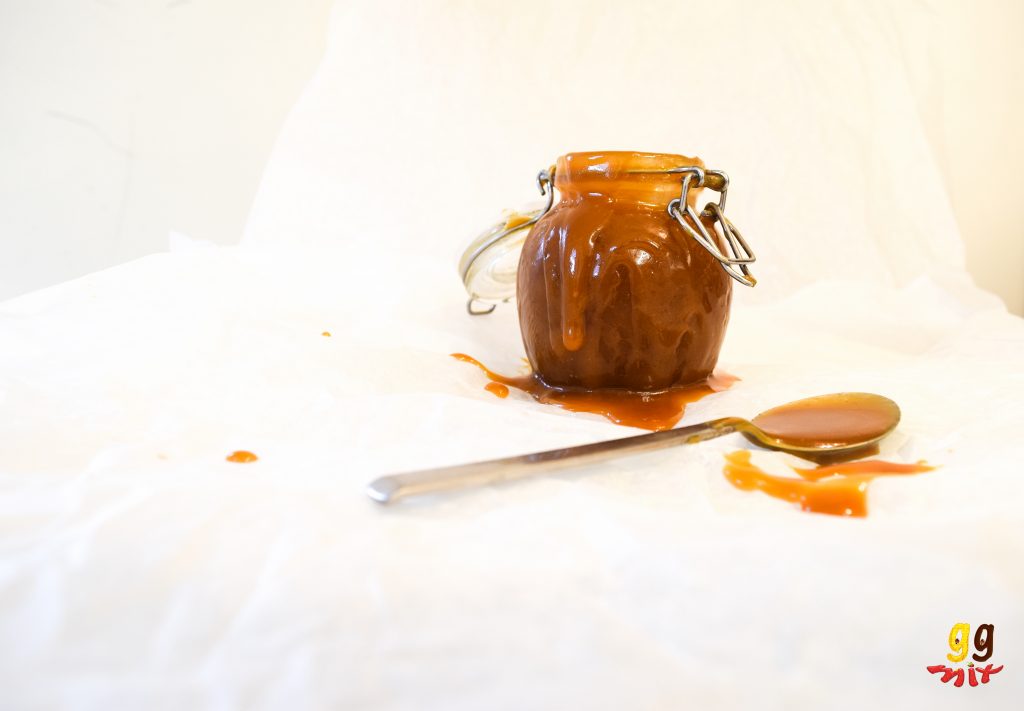 a jar of salted caramel with caramel spilling out and a spoon covered with caramel making a mess