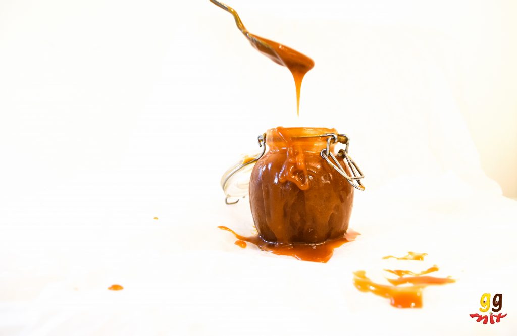 a spoon of salted caramel dripping off of a spoon into a jar
