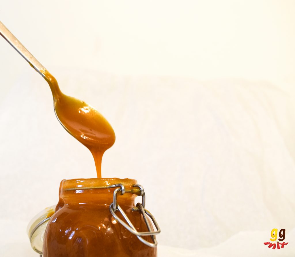 a spoon of salted caramel sauce dripping off of a spoon into a jar