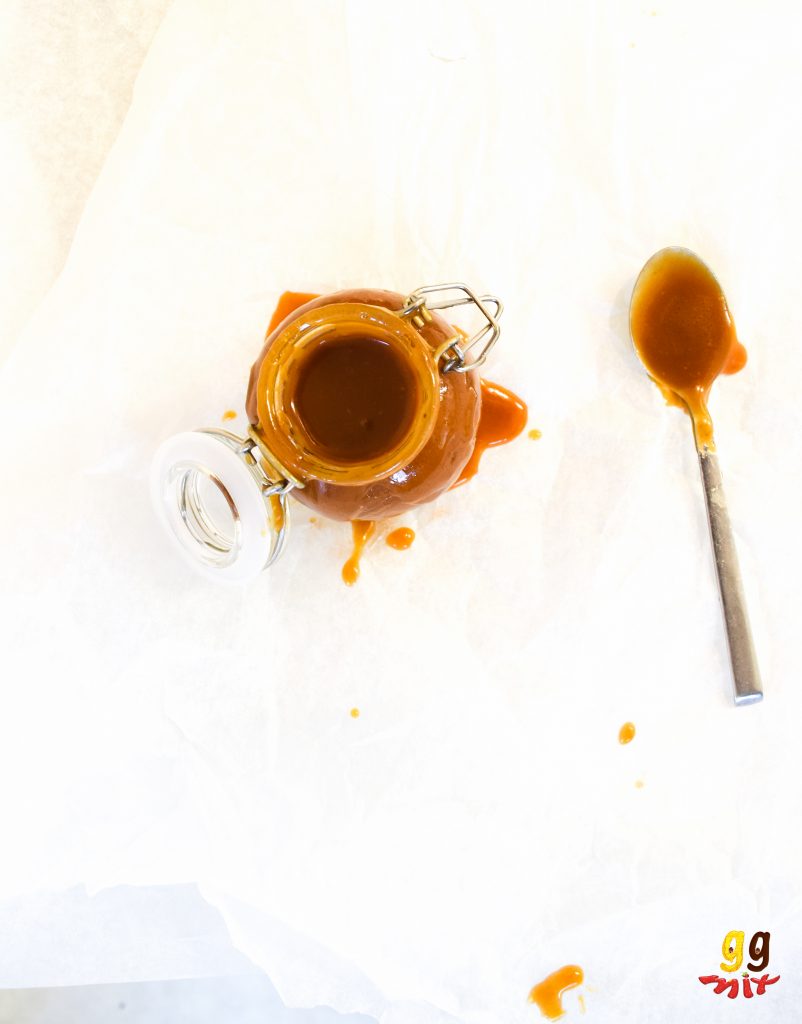 a view from above of a jar of salted caramel and a spoon covered with caramel making a mess