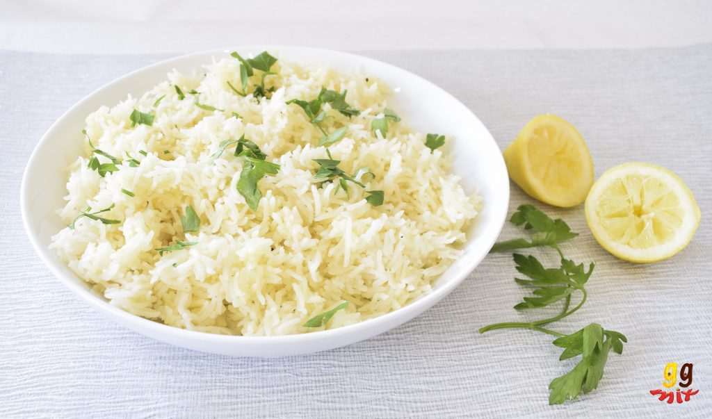 a bowl of lemon rice sprinkled with parsley and 2 squeezed lemon halves on the side