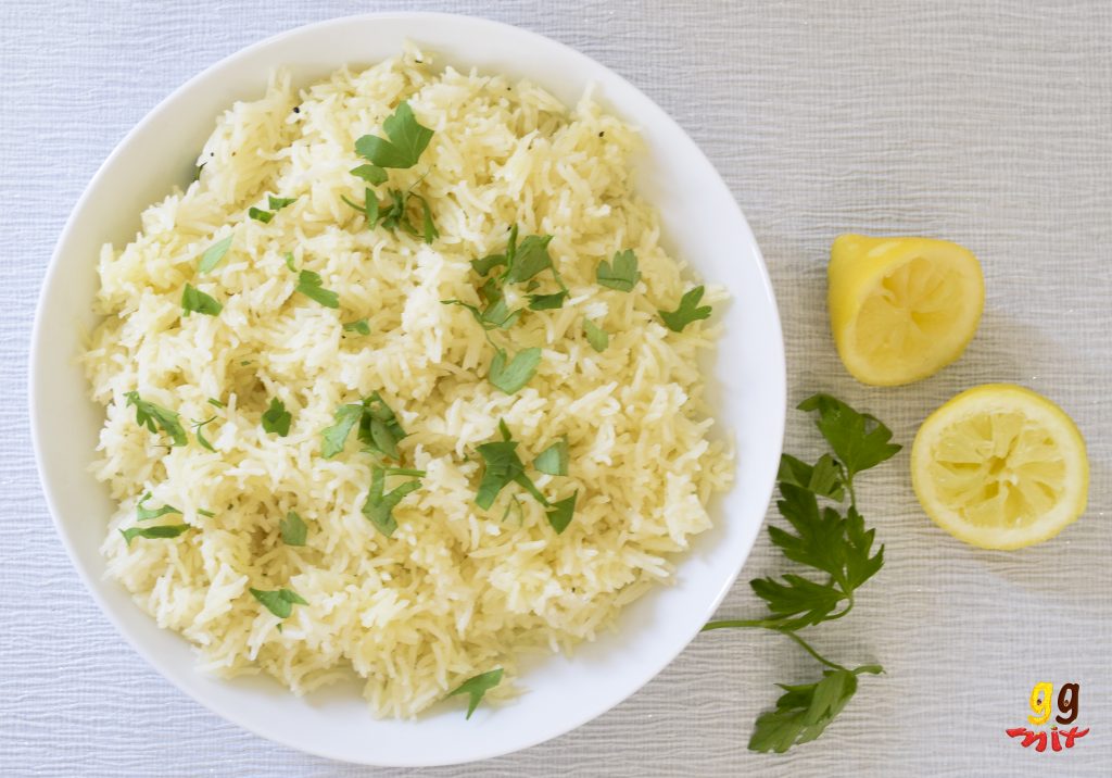 a bowl of lemon rice sprinkled with parsley and 2 squeezed lemon halves on the side