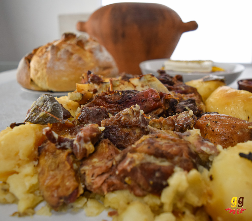 kleftiko slow cooked lamb and potatoes on a platter, Greek village bread and a traditional Greek kleftiko clay pot