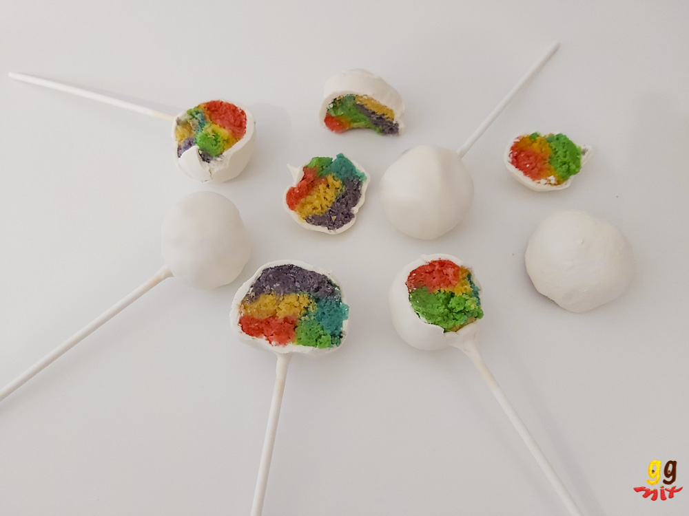 5 cake pops. 3 are in half and reveal a rainbow coloured center and 2 are still whole with a white chocolate coating plus half a rainbow truffle