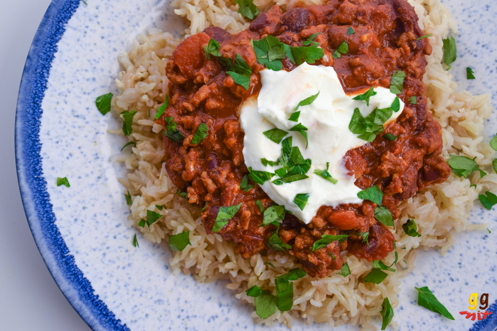 a plate of brown rice and chilli con carne topped with some Greek yogurt in the middle and a sprinkling of chopped parsley