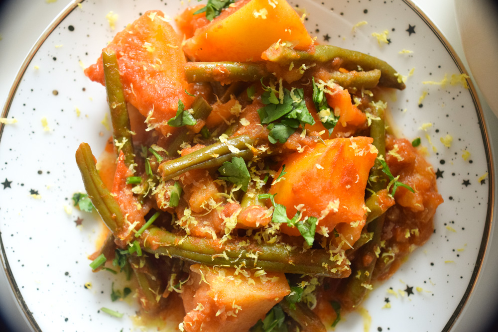 a plate of fasolakia green beans and potatoes in a tomatoe sauce topped with lemon zest and parsley