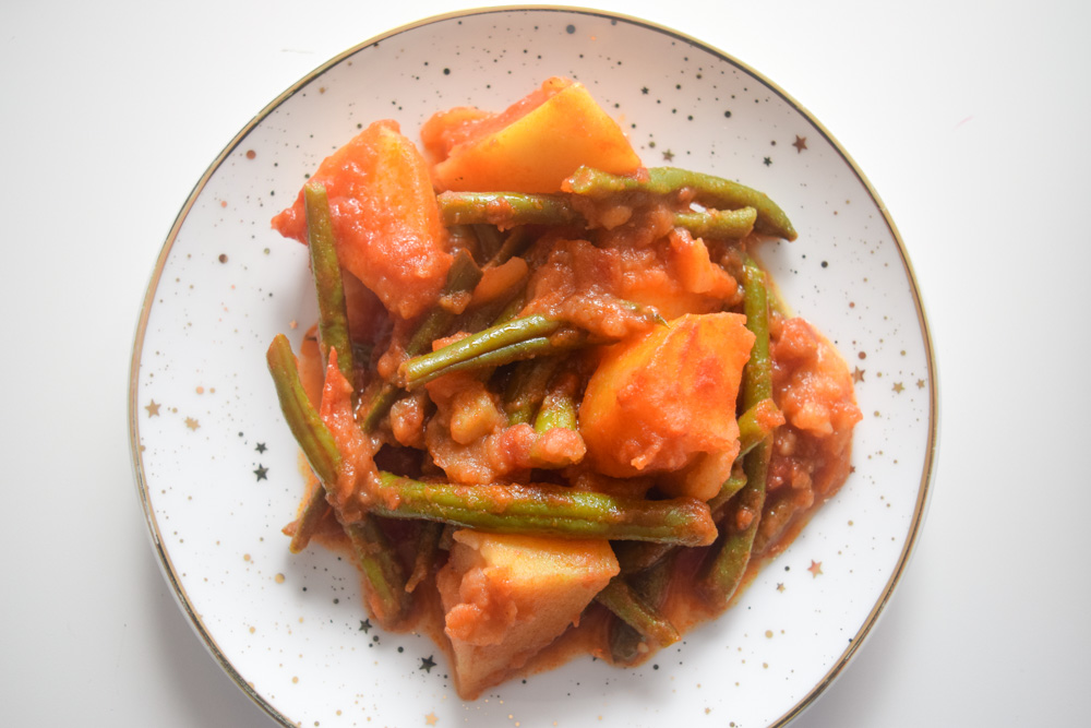 a plate of fasolakia green beans and potatoes in a tomatoe sauce